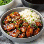 Air fryer teriyaki chicken served with white rice in a grey bowl, garnished with sesame seeds and chopped green onions.