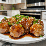 Juicy pineapple teriyaki chicken meatballs glazed in a rich sauce, garnished with sesame seeds and chopped green onions on a white plate.